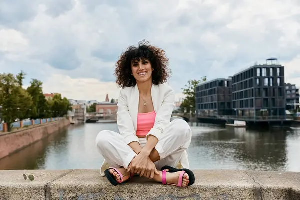 stock image A woman in stylish attire sits on a bridge overlooking a European canal.