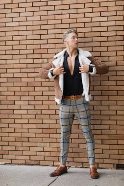 A handsome blonde man in stylish attire stands against a brick wall on the streets of Orlando, Florida. clipart