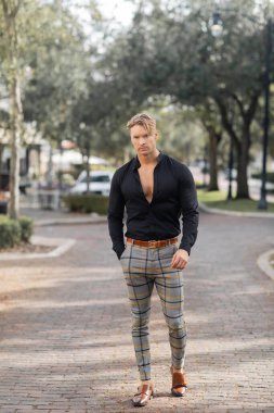 Siyah gömlekli ve ekose pantolonlu yakışıklı sarışın bir adam Orlando, Florida 'da sokakta yürüyor..