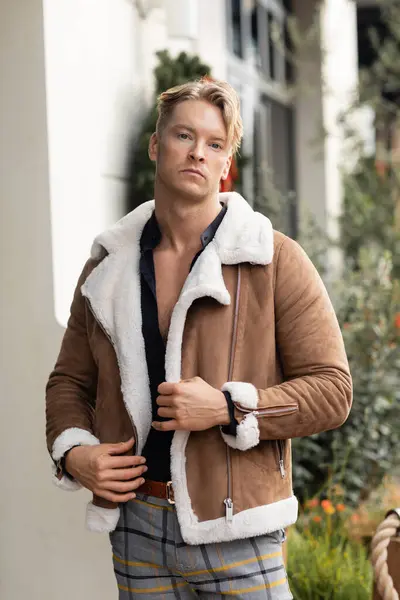 stock image A handsome blonde man in a stylish brown jacket stands on a street in Orlando, Florida.