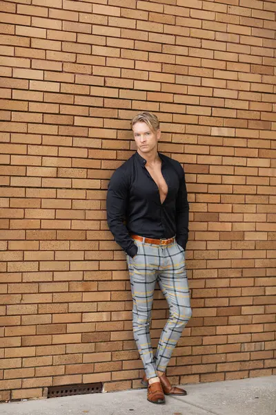 stock image A handsome blonde man in stylish attire poses against a brick wall
