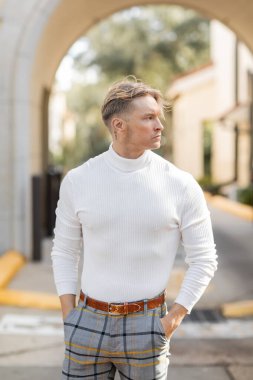 Beyaz balıkçı yaka ve ekose pantolon giyen sarışın bir adam güneşli bir Florida caddesinde poz veriyor..