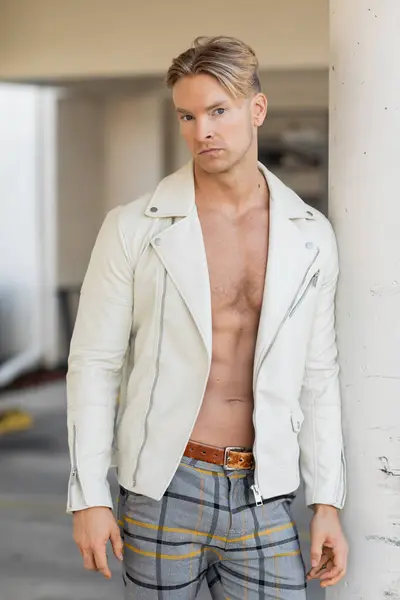 stock image A handsome blonde man poses in a white leather jacket and plaid pants on a street in Florida.