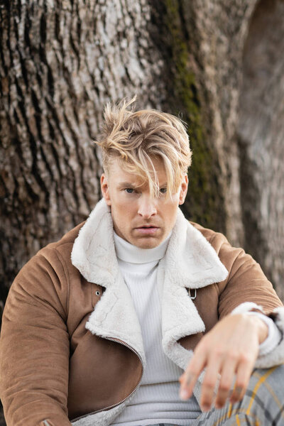 Стильно одетый блондин в зеленом парке Майами, излучающий уверенность и урбанистическое спокойствие..