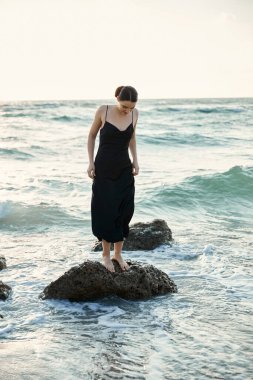 Güneş Miami sahilinin üzerinde batarken siyah elbiseli genç bir kadın dalgaların üzerinde duruyor..