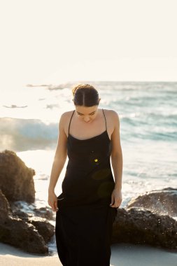 A young woman in a black sundress walks along the shore of Miami Beach, Florida. clipart