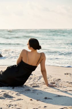 Siyah elbiseli genç bir kadın kumda oturuyor, okyanus dalgalarına bakıyor, Miami Beach, Florida 'da..