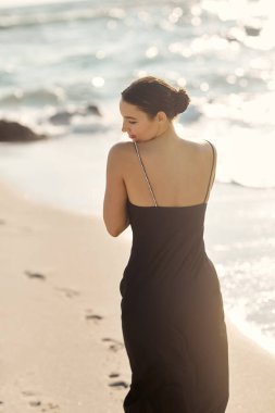 Siyah elbiseli genç bir kadın Miami, Florida sahillerinde yürüyor..