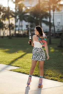 Güneş gözlüklü ve çiçekli etekli genç bir kadın Miami 'de güneşli bir öğleden sonra paten kayıyor..