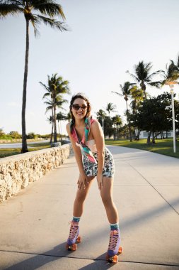 Güneş gözlüklü ve şık kıyafetli genç bir kadın Miami 'de asfalt bir patika boyunca paten kayıyor..