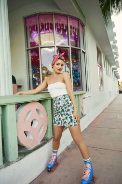 Güneş gözlüklü ve şık giyinmiş genç bir kadın Miami 'de pembe ve yeşil bir binanın önünden geçiyor..