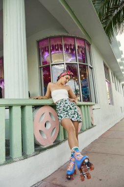 Güneş gözlüklü ve çiçekli etekli genç bir kadın Miami sokaklarında kayıyor..