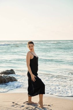 Siyah elbiseli genç bir kadın Miami Beach, Florida kıyılarında yürüyor..