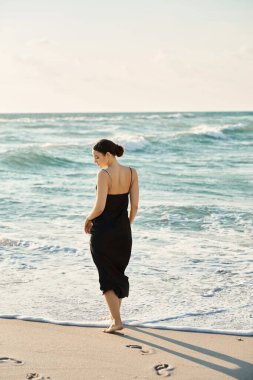 Miami Plajı 'nda, siyah elbiseli bir kadın sahilde yürüyor, ayaklarında okyanus dalgalarını hissediyor..