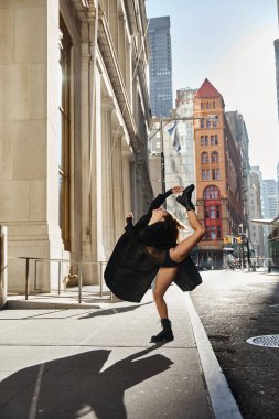 A young woman dances on a city street in New York, displaying impressive flexibility. clipart