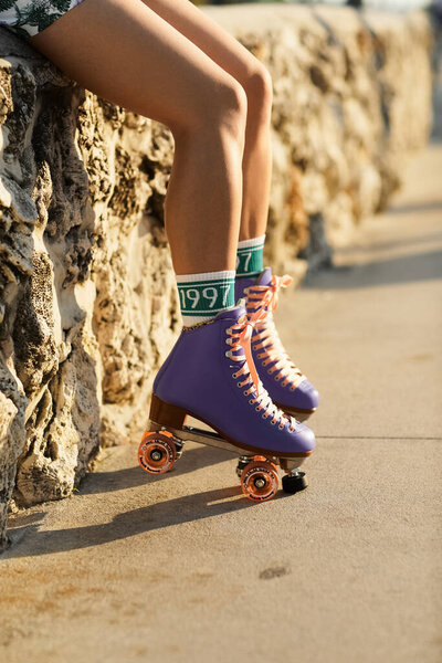 Молодая женщина сидит на каменной стене в роликовых коньках, наслаждаясь закатом в Майами.