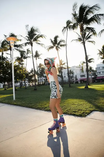 stock image A young woman wearing sunglasses and a stylish headscarf rollerblades down a Miami sidewalk.