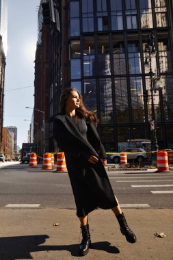 New York 'ta bir sokakta dans eden genç bir kadın, rüzgarda dalgalanan siyah paltosu.