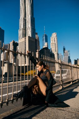 Kadın New York kaldırımında oturuyor, gökdelenlerin ortasında düşüncelere dalmış..