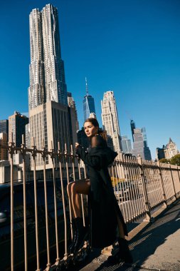 Siyah paltolu genç kadın New York caddesinde dans ediyor, gökdelenler ve metal çitler arka planda.