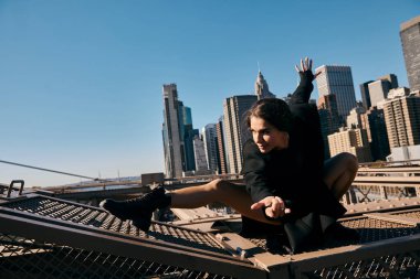 Siyah ceketli genç bir kadın New York 'taki Brooklyn Köprüsü' nde dans ediyor..