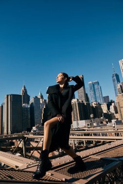 Brooklyn Köprüsü 'nde siyah ceketli bir kadın dans ediyor. Arka planda New York silüeti var..