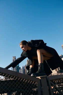 Siyah ceketli genç bir kadın New York 'ta bir köprüde dans ediyor..