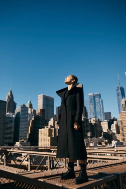 Siyah ceketli genç bir kadın New York 'ta bir köprüde dans ediyor..