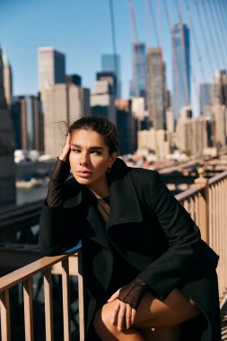 Siyah paltolu genç bir kadın New York 'ta bir korkulukta oturuyor..
