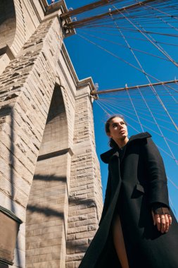 Brooklyn Köprüsü 'nün zemininde siyah paltolu bir kadın duruyor..