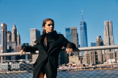 Siyah ceketli bir kadın New York şehrinin siluetine karşı poz veriyor..