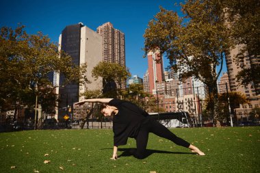 Genç bir kadın New York City gökdelenleriyle çevrili bir parkta dans ediyor..
