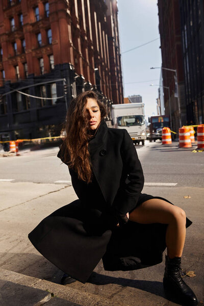 A young woman dances on the streets of New York City, wearing a long black coat.