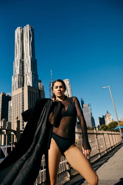 Young woman in black outfit dancing in NYC with skyscraper in background.
