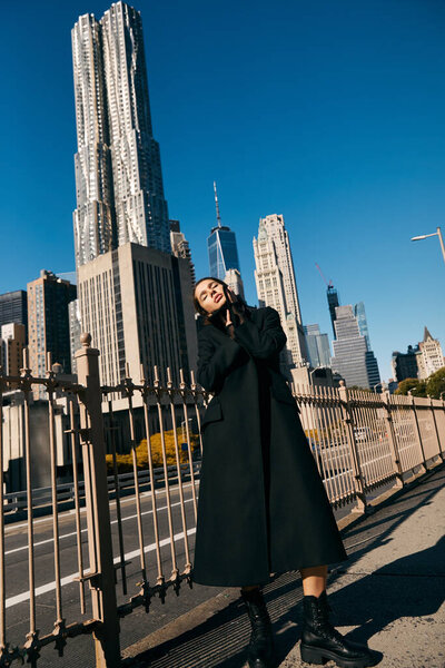 Young woman in black coat dances on NYC street with skyscrapers.
