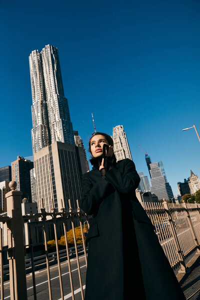 Молодая женщина позирует на улице Нью-Йорка, демонстрируя силуэт города на заднем плане.