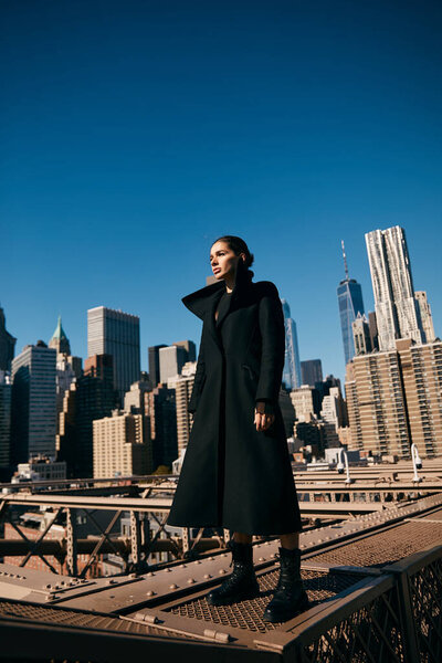 Молодая женщина стоит на мосту в Нью-Йорке, ее силуэт обрамлен высокими зданиями.