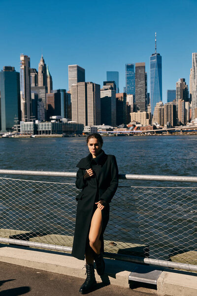 A young woman in a black coat poses against the iconic skyline of New York City.