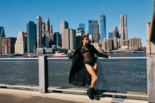 Молодая женщина в черном танцует на пирсе с видом на Нью-Йорк.