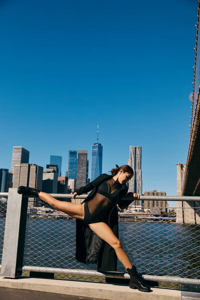 Woman in black bodysuit splits on railing with NYC skyline.