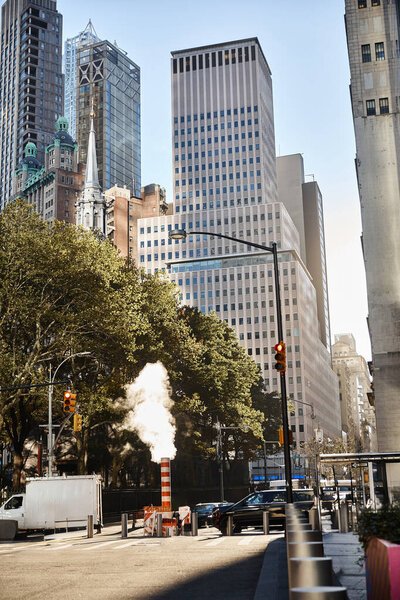 A bustling street in New York City with a plume of steam rising from the sidewalk.