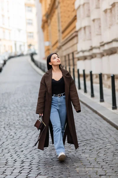 Повна довжина жінки в стильному пальто джинси, що ходять в празі і дивляться в сторону — стокове фото