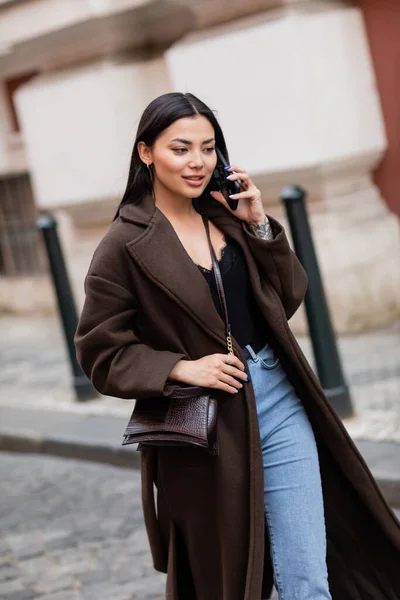 Positive and stylish brunette woman talking on smartphone on street in prague — Stock Photo