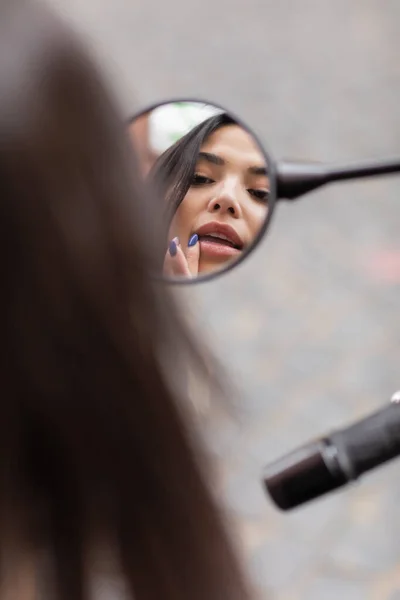 Mulher morena com maquiagem olhando no espelho e tocando os lábios ao ar livre — Fotografia de Stock