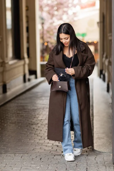 Femme brune à la mode prenant téléphone portable de bandoulière dans la rue à la prague — Photo de stock