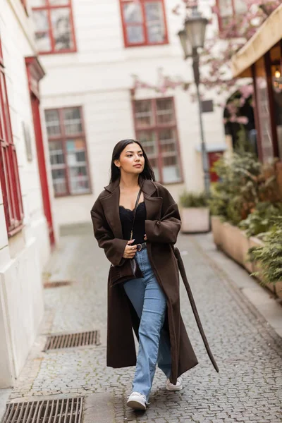 Full length of young woman in trendy autumn clothes walking along narrow street in prague — Stock Photo