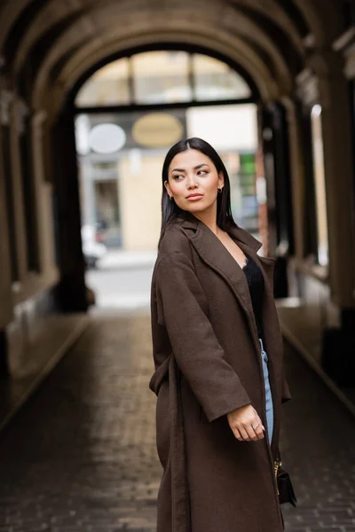 Bella donna bruna in cappotto alla moda guardando lontano vicino edificio arco sfocato a Praga — Foto stock