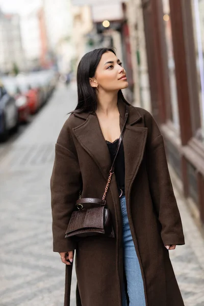 Красивая брюнетка в коричневом пальто с модным перекрестным телом, смотрящая на городскую улицу в Праге — стоковое фото
