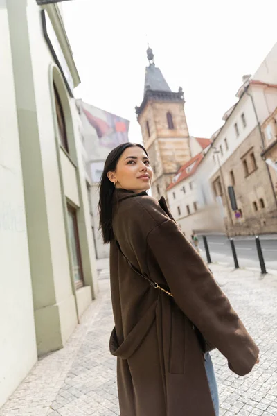 Jeune femme brune en vêtements d'automne debout et regardant loin dans la prague sur la rue antique — Photo de stock