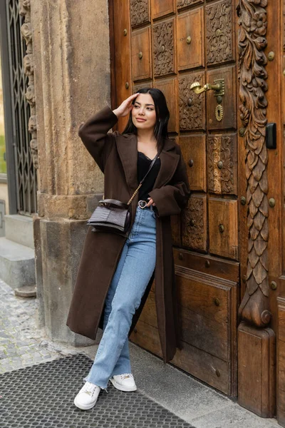 Lächelnde Frau in Jeans und Mantel mit Haaren in der Nähe einer geschnitzten Holztür in Prag — Stockfoto